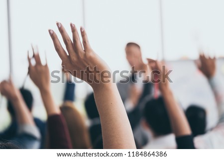 Audience raising hands up while businessman is speaking in training at the office.