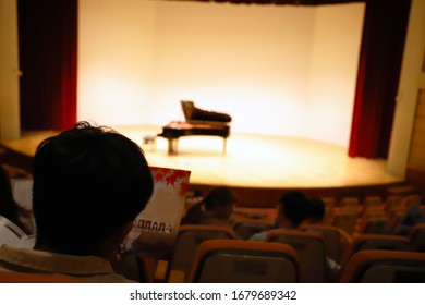 The Audience Is Reading The Pamphlets At The Piano Concert, Waiting For The Arrival Of The Performers.