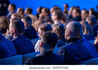 Audience sitting and attentively listening to a speaker during a business conference. The image captures a professional atmosphere with engaged participants.