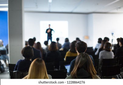 Audience Watching A Presentation. Blurred Presenter At Conference Meeting Tech Event. Technology Executive Manager Speaker On Stage At Global Business Conference Presenting Education Seminar.