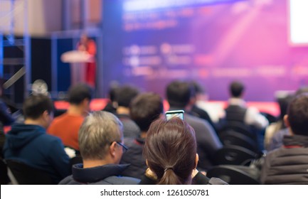 Audience Watching A Presentation. Business. Female Presenter On Stage Giving Talk To Crowd Of People. Woman Speaker At  Investor Pitch Conference. 
Defocused Blurred Presenter During Conference.