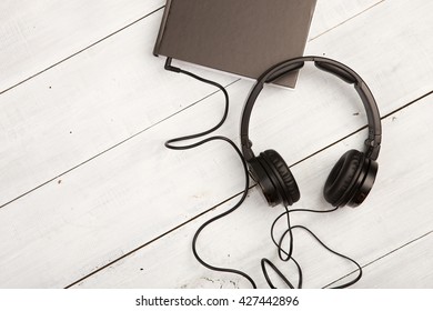 Audio Book Concept With Black Book And Headphones On White Wooden Background