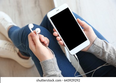 Audio book concept. Young woman holding smart phone and earphones, close up - Powered by Shutterstock