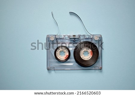 Audio cassette with torn tape on a blue background, top view.
