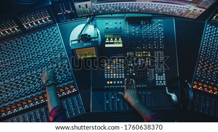 Audio Engineer, Musician, Artist Works in the Music Record Studio, Control Desk Mixer with Equalizer. Hand Moving Fader, Buttons to Broadcast, Record, Play Song. Neon Colors. Top Down View