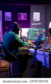 Audio engineer working in home studio with digital software on pc, playing piano keys and editing audio recordings. Musician producer creating tracks on midi controller keyboard notes.