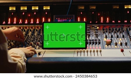 Audio expert mixing and mastering tunes on editing software next to greenscreen tablet, producing and recording tracks by pushing buttons and faders. Sound engineer in control room. Camera A.