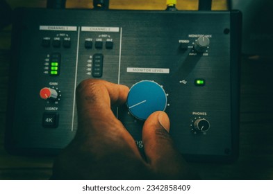 Audio interface with a man's left hand fine-tuning a dial while audio meters to the left of his hand illuminate gree.