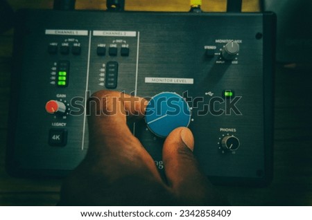 Audio interface with a man's left hand fine-tuning a dial while audio meters to the left of his hand illuminate gree.