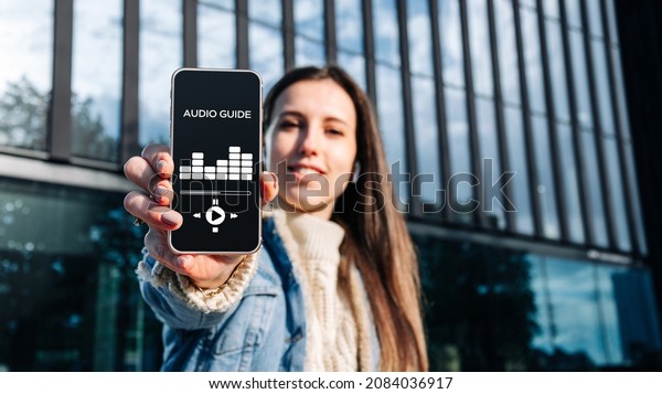 Audio tour online app on digital mobile\
smartphone. Happy young student woman holding phone listening\
audioguide. Simultaneous translation\
devices