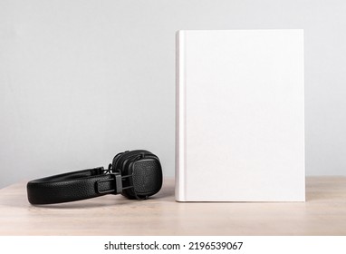 Audiobook Concept. Headphones And Book Mockup With White Blank Cover At Wooden Table. Novel Listening Or Reading. Literature Advertising. High Quality Photo