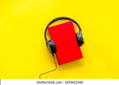Audiobooks concept. Headphones put over hardback book. Yellow background top view copy space

