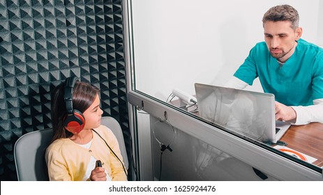 Audiologist Doing A Hearing Test Of The Child. Girl Complaining Of Bad Hearing