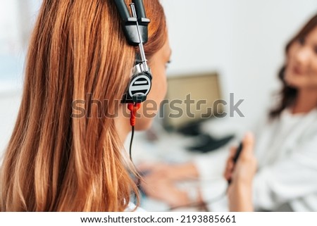 Audiologist doing impedance audiometry or diagnosis of hearing impairment. An beautiful redhead adult woman getting an auditory test at a hearing clinic. Close up shot.