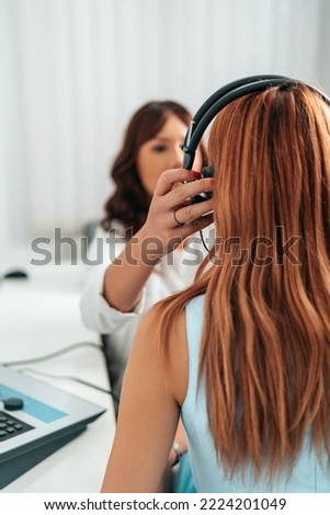 Audiologist doing impedance audiometry or diagnosis of hearing impairment. An beautiful redhead adult woman getting an auditory test at a hearing clinic.