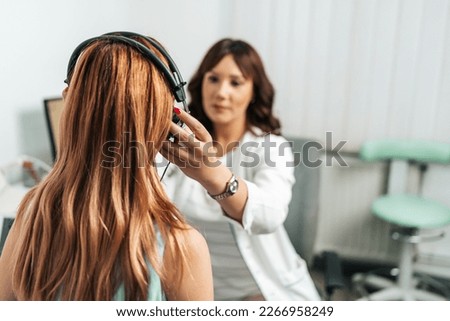 Audiologist doing impedance audiometry or diagnosis of hearing impairment. An beautiful redhead adult woman getting an auditory test at a hearing clinic.