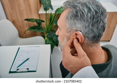 Audiologist Fits A Hearing Aid On Deafness Mature Man Ear While Visit A Hearing Clinic. Hearing Solutions For Older