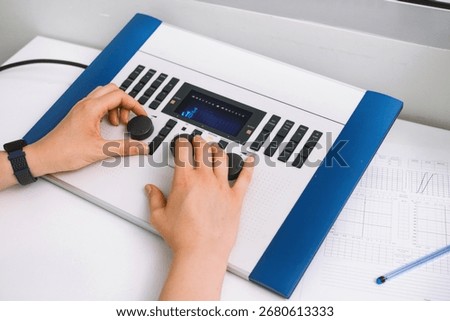 Audiologist operates audiometer and computer, analyzing hearing test results in modern clinic. Medical diagnosis, audiology, ENT, pure tone audiometry. Close-up