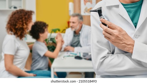 Audiologist With Otoscope Over Background Consultation Doctor With Child Patient And His Mother At Hearing Clinic. Ear Treatment And Hear Exam