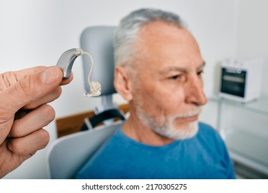 Audiologist presents BTE hearing aid for mature hearing impaired man to treat his deafness, close-up. Audiology, auditory solutions - Shutterstock ID 2170305275