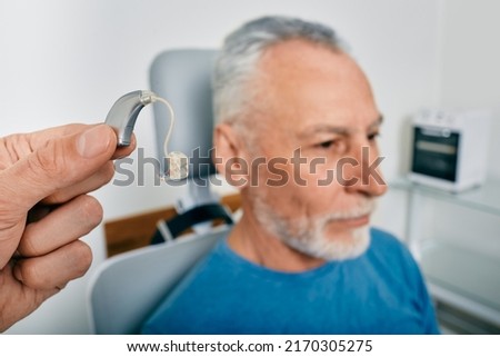 Audiologist presents BTE hearing aid for mature hearing impaired man to treat his deafness, close-up. Audiology, auditory solutions