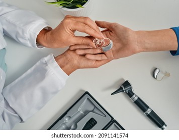 Audiologist puts modern BTE hearing aid in patient hand for treatment deafness at hearing clinic, top view. Hearing solutions
