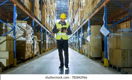 Auditor Wearing Hard Hat with Tablet Computer Counts Merchandise in Warehouse. He Walks Through Rows of Storage Racks with Merchandise.