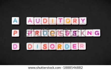 Auditory processing disorder and short form APD spelled out in colorful block letters on black textured fabric background. Also known as central auditory processing disorder or CAPD.