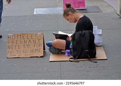 August 20, 2020: Homeless White Woman Sitting On Cardboard Reading A Book On The Side Walk In The Middle Of Time Square Midtown Manhattan New York.