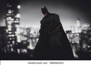 AUGUST 21 2020: Batman from DC Comics looming over Gotham City at night - Mattel action figure
