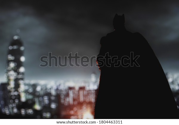 AUGUST 21 2020: Batman from DC\
Comics looming over Gotham City at night - Mattel action\
figure