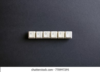 August month word is written with computer keys button. Flat lay view from above on the table with computer keyboard keys buttons on a dark background.