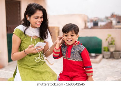 An aunt listening music and sharing headphones with her cute little nephew. They are sitting together and enjoying their leisure time. She is wearing traditional Indian dress salwar Kameez and Dupatta - Shutterstock ID 1683842545