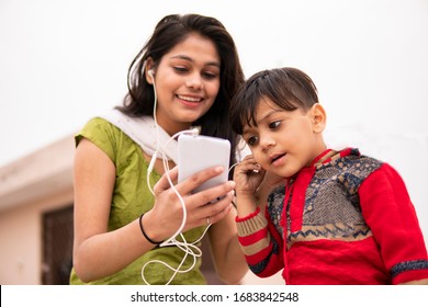 An aunt listening music and sharing headphones with her cute little nephew. They are sitting together and enjoying their leisure time. She is wearing traditional Indian dress salwar Kameez and Dupatta - Shutterstock ID 1683842548