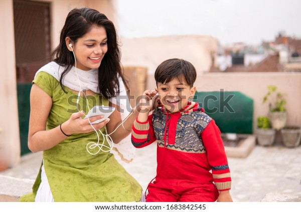 An aunt listening music and sharing headphones\
with her cute little nephew. They are sitting together and enjoying\
their leisure time. She is wearing traditional Indian dress salwar\
Kameez and Dupatta