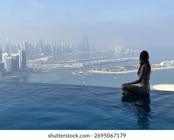 Aura skypool view, infinity pool, a woman sits by the edge, taking in the breathtaking view of the city and the ocean