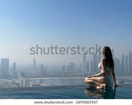 Aura skypool view, infinity pool, a woman in a bikini sits by the pool, overlooking the skyline of Dubai on a bright, sunny day