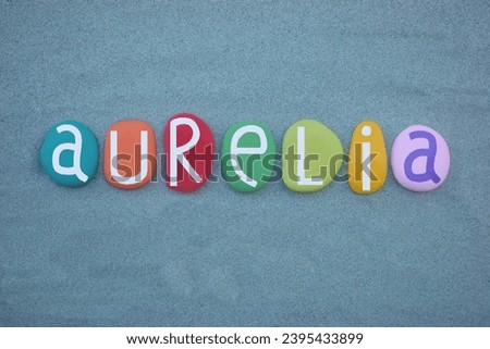 Aurelia, feminine given name composed with multi colored stone letters over green sand