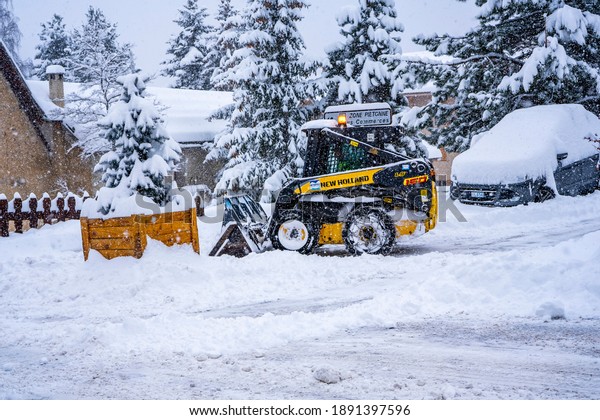Auron, France - 01.01.2021: Wheel loader machine\
removing snow on a ski resort. Clearing the road from snow. High\
quality photo