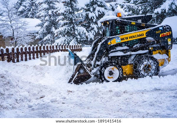 Auron, France - 01.01.2021: Wheel loader machine\
removing snow on a ski resort. Clearing the road from snow. High\
quality photo