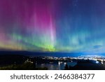 Aurora Australis or southern lights over the city of Dunedin, New Zealand; beautiful purple, pink and green lights, with city light, clouds, ocean and night sky in the background