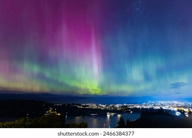 Aurora Australis or southern lights over the city of Dunedin, New Zealand; beautiful purple, pink and green lights, with city light, clouds, ocean and night sky in the background - Powered by Shutterstock