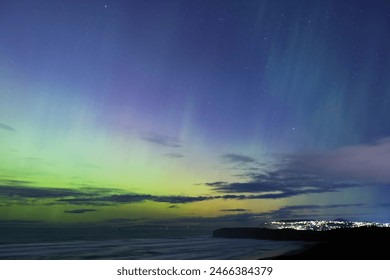 Aurora Australis or southern lights over the city of Dunedin, New Zealand; beautiful purple, pink and green lights, with city light, clouds, ocean and night sky in the background - Powered by Shutterstock