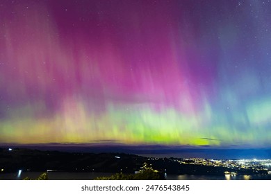 Aurora Australis or southern lights over the city of Dunedin, New Zealand; beautiful purple, pink and green lights, with city light, clouds, ocean and night sky in the background - Powered by Shutterstock