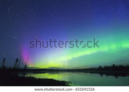 Aurora Borealis glowing green in night sky full of stars, pink color bursting up from left horizon