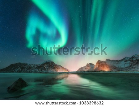 Aurora borealis in Lofoten islands, Norway. Aurora. Green northern lights. Starry sky with polar lights. Night winter landscape with aurora, sea with sky reflection, stones, beach and snowy mountains