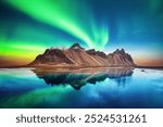 Aurora borealis Northern lights over famous Stokksnes mountains on Vestrahorn cape. Reflection in the clear water on the epic skies background, Iceland. Landscape photography