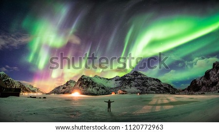 Aurora borealis (Northern lights) over mountain with one person at Skagsanden beach, Lofoten islands, Norway