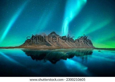 Aurora borealis Northern lights over famous Stokksnes mountains on Vestrahorn cape. Reflection in the clear water on the epic skies background, Iceland. Landscape photography
