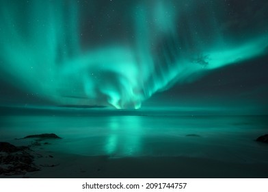 Aurora borealis over the sea. Northern lights in Lofoten islands, Norway. Starry sky with polar lights. Night landscape with aurora, sea with blurred water and sky reflection, sandy beach. Aurora  - Shutterstock ID 2091744757
